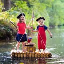 A young boy and young girl dressed pirates float down the river while standing on a wooden raft