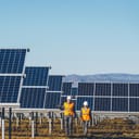 Two workers with helmets walking through a solar panel farm