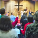 Christian congregation worshipping together with a cross emitting light rays in the background