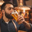 a man with a beard tasting beer from a glass