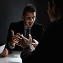 Man talking to a handcuffed person within a dimly lit room