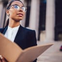 a woman wearing glasses and holding documents in her hand