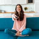 A smiling young woman sitting on a couch holding a remote control