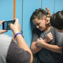 Boy being bullied by another boy while another one records the bullying with smartphone