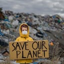 A child with a face mask holding a Save our planet board at a landfill
