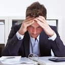 A worried business man sitting at table looking at records with hands on his head