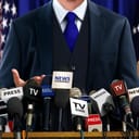 A politician holding a press conference with a lot of microphones in front of him