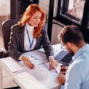 two business professionals, a man and a woman, sitting at an office table, finalizing and signing a contract