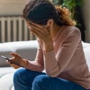 Woman sitting on couch tiringly using her smartphone