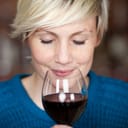 a closeup of a woman savoring red wine with her eyes closed