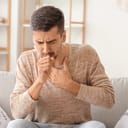 A man sitting on a couch coughing