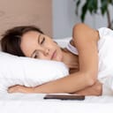Woman in bed glancing at a smartphone by her side