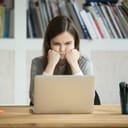 young female office worker staring at a laptop with a frown, disappointed by something she's reading
