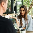 A confused young woman gestures with her hand while looking at her boyfriend.