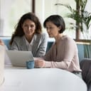 Two women collaborating at the office, focusing on a laptop screen as they navigate new software. 