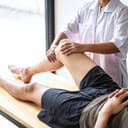 A female physiotherapist examines and treats the injured leg of a male patient during rehabilitation therapy in a clinic setting.
