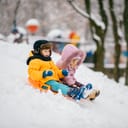 A boy and a girl sliding down a slope on a sled