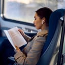 An over the shoulder view of a young woman reading a book on a bus