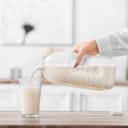 A woman pouring milk into a glass from a large plastic bottle