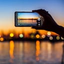 Closeup of a woman's hand holding a smartphone trying to capture panoramic view of the background at dusk
