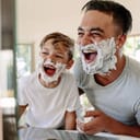 Father and son playing around in bathroom with shaving foam on their faces