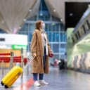 woman with yellow suitcase and mask on her face standing at empty airport check-in counters during COVID-19 pandemic