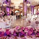 a dinner table for a wedding reception decorated with a garland of pink and white flowers, looking into a luxurious dinner hall