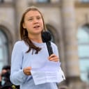 Greta Thunberg holding a piece of paper and talking into a microphone