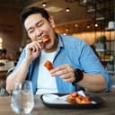Happy Asian man eating BBQ chicken wings in restaurant.