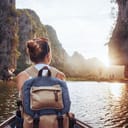 A woman with a backpack sitting in a boat looking at a sunset
