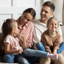 Happy parents with two young daughters sharing a tender moment on the couch, smiling and enjoying family time together