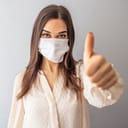 Woman wearing a face mask gives a thumbs up