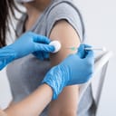 Close-up of a patient's arm while a doctor or nurse is injecting a vaccine using a syringe.