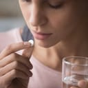 Close up cropped image millennial mixed race girl holding pill and glass of fresh water, taking medicine from head ache, stomach pain or taking vitamins, sedation meds, healthcare concept
