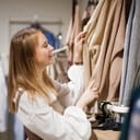 happy young woman girl chooses beige knitwear clothes for autumn or winter in clothing store. shopping in shop.