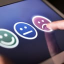 A person giving a negative rating by tapping a sad face on a tablet