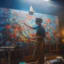 A skilled female artist paints an abstract oil piece with sweeping brush strokes on a big canvas in her studio.