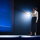 On-Stage Successful Female Speaker Presents Technological Product, Uses Remote Control for Presentation, Showing Infographics, Statistics Animation on Screen. Live Event / Device Release.