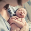 Newborn baby sleeping in their mother's arms as she looks on