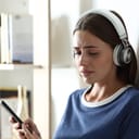 young woman with headphones on, listening to music and crying while sitting in her bedroom