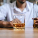 A glass of whisky on table in front of a person sitting