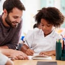 Male elementary school teacher giving female pupil Wearing a uniform a one to one support In classroom