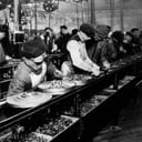 Workers on the first moving assembly line put together magnetos and flywheels for 1913 Ford autos" Highland Park, Michigan