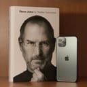 iPhone next to Steve Jobs book on a wooden table