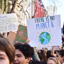 People holding signs at a climate protest. The sign in focus reads "There is no Planet B"