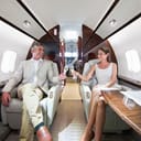A rich couple sitting in a private jet airplane drinking champagne