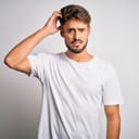 Young handsome man with beard wearing casual t-shirt standing over white background confuse and wonder about question. Uncertain with doubt, thinking with hand on head. Pensive concept.