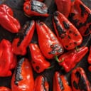 Close-up of red peppers roasting on a wood-burning stove, showing their charred surface.