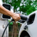 Close-up of a person's hand plugging an EV charger into a white electric vehicle.