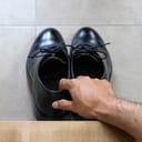 close-up of a man picking up or leaving black business shoes at an entrance